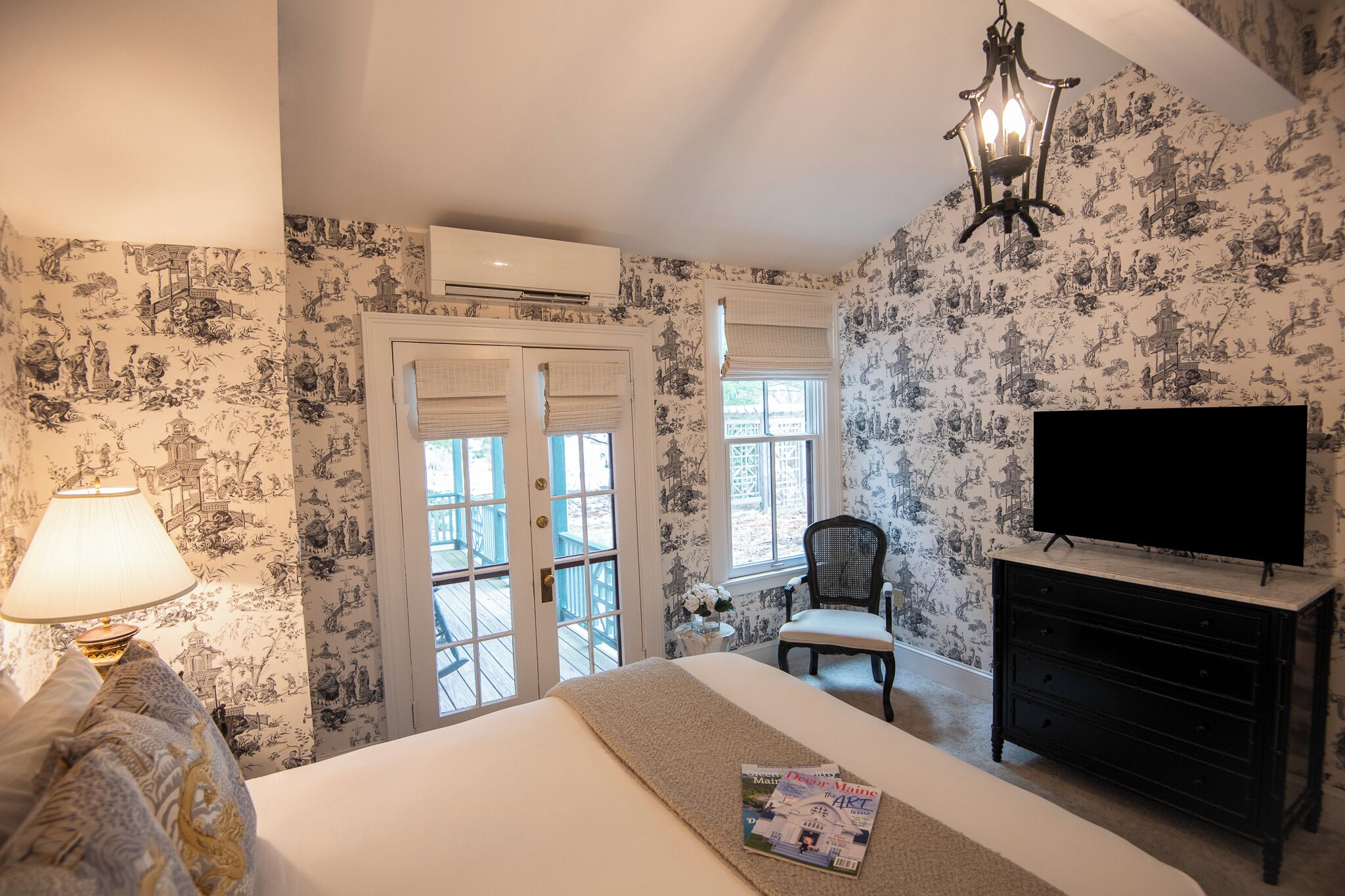 Een slaapkamer met een bed, een televisie, een dressoir, een stoel en een raam met uitzicht op een balkon.