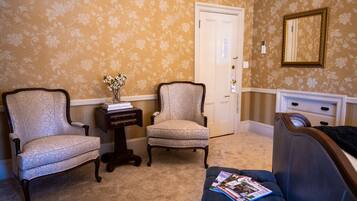 A room with two armchairs, a small table with a vase, a blue sofa with magazines, a door, and a dresser.