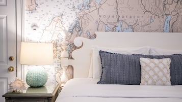 Quarto com parede de mapa, cama com almofadas azuis e bege, abajur e concha decorativa na mesa de cabeceira.