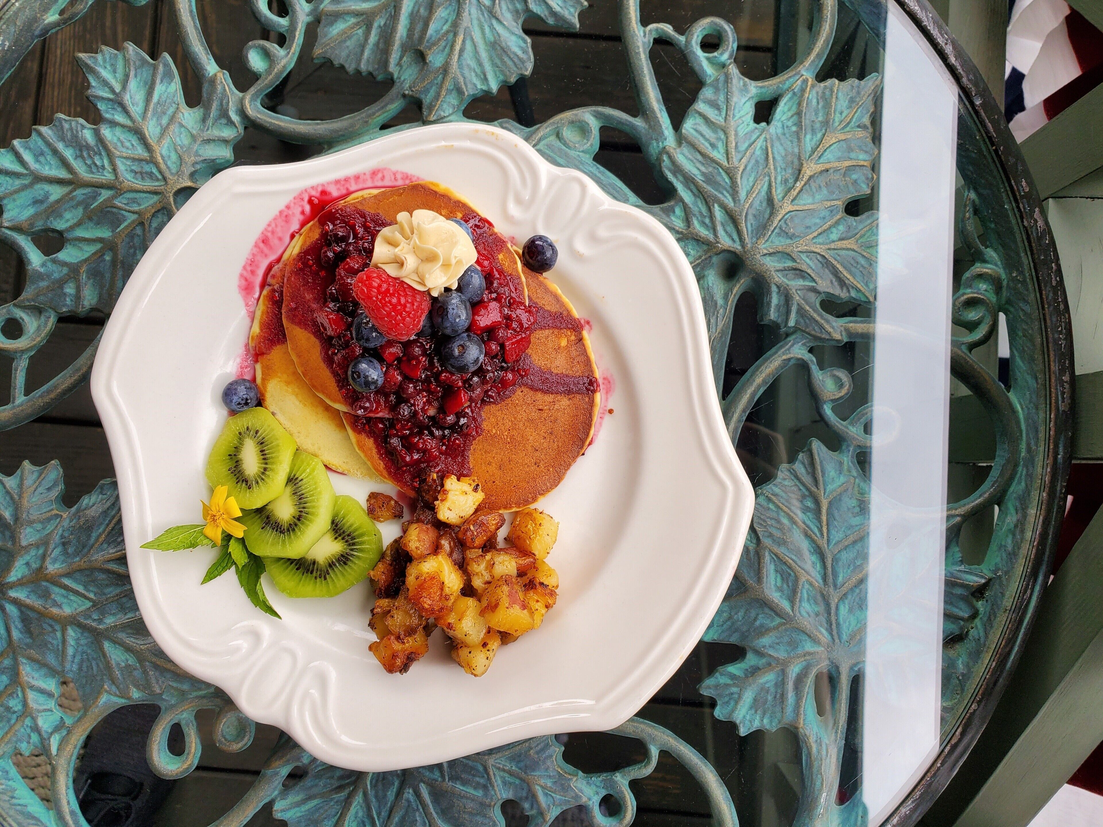 A breakfast plate with pancakes, berries, kiwi, and fried potatoes on a decorative table.
