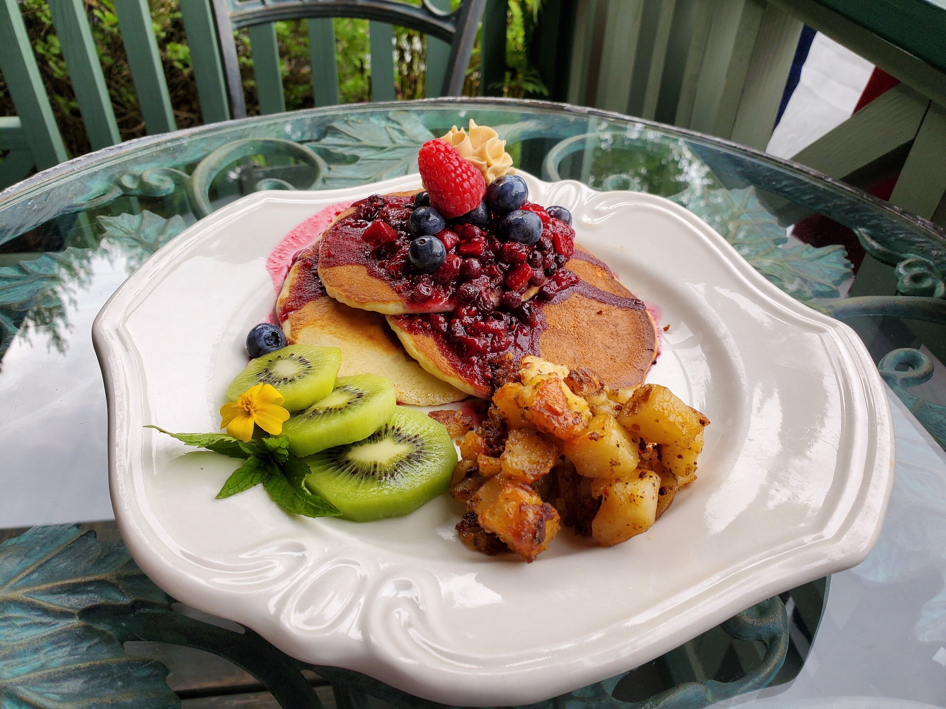 Une assiette de petit-déjeuner avec des crêpes, des baies, des tranches de kiwi et des pommes de terre.