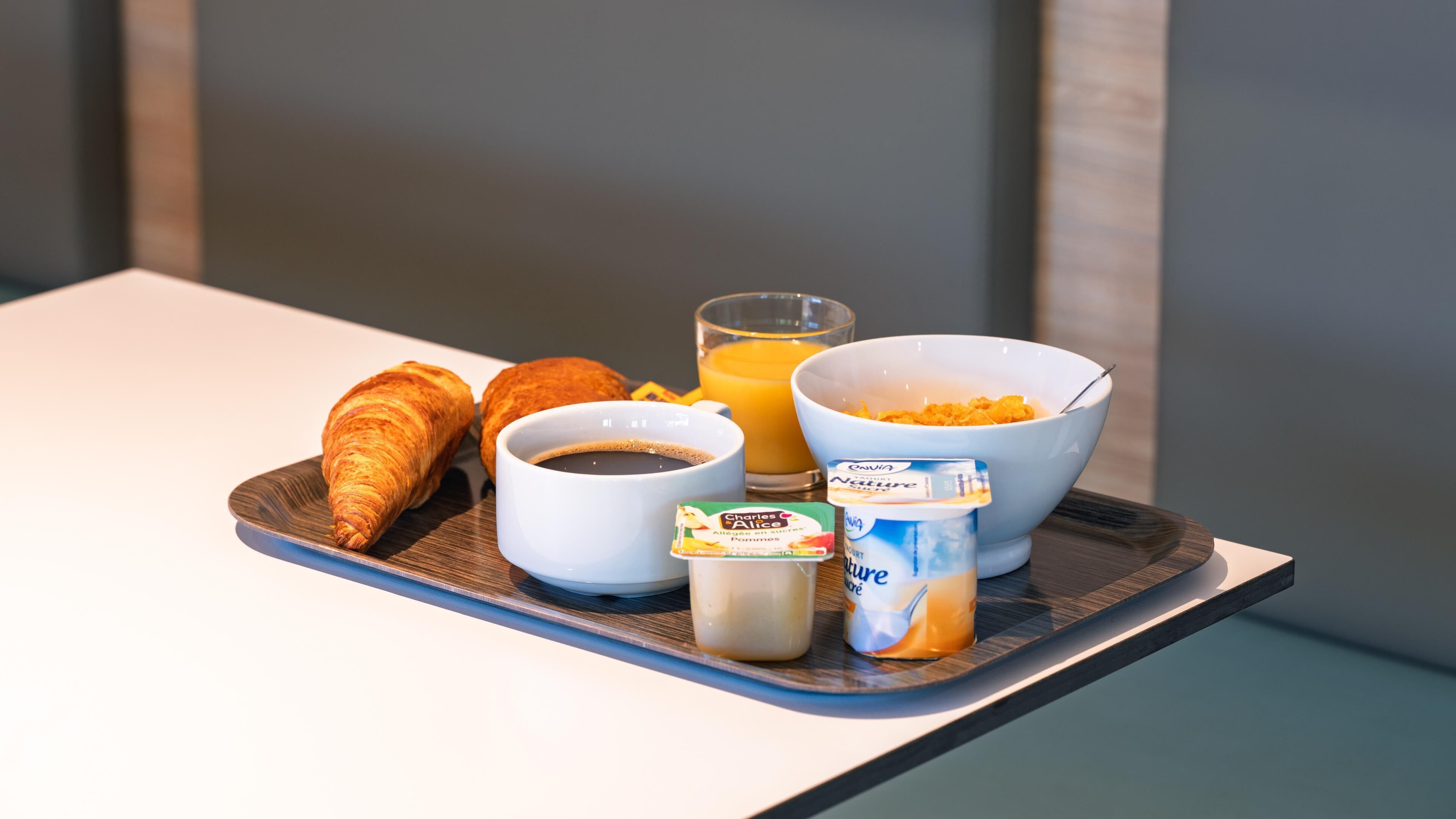 Una bandeja de desayuno con cruasanes, café, zumo de naranja y yogur sobre una mesa.