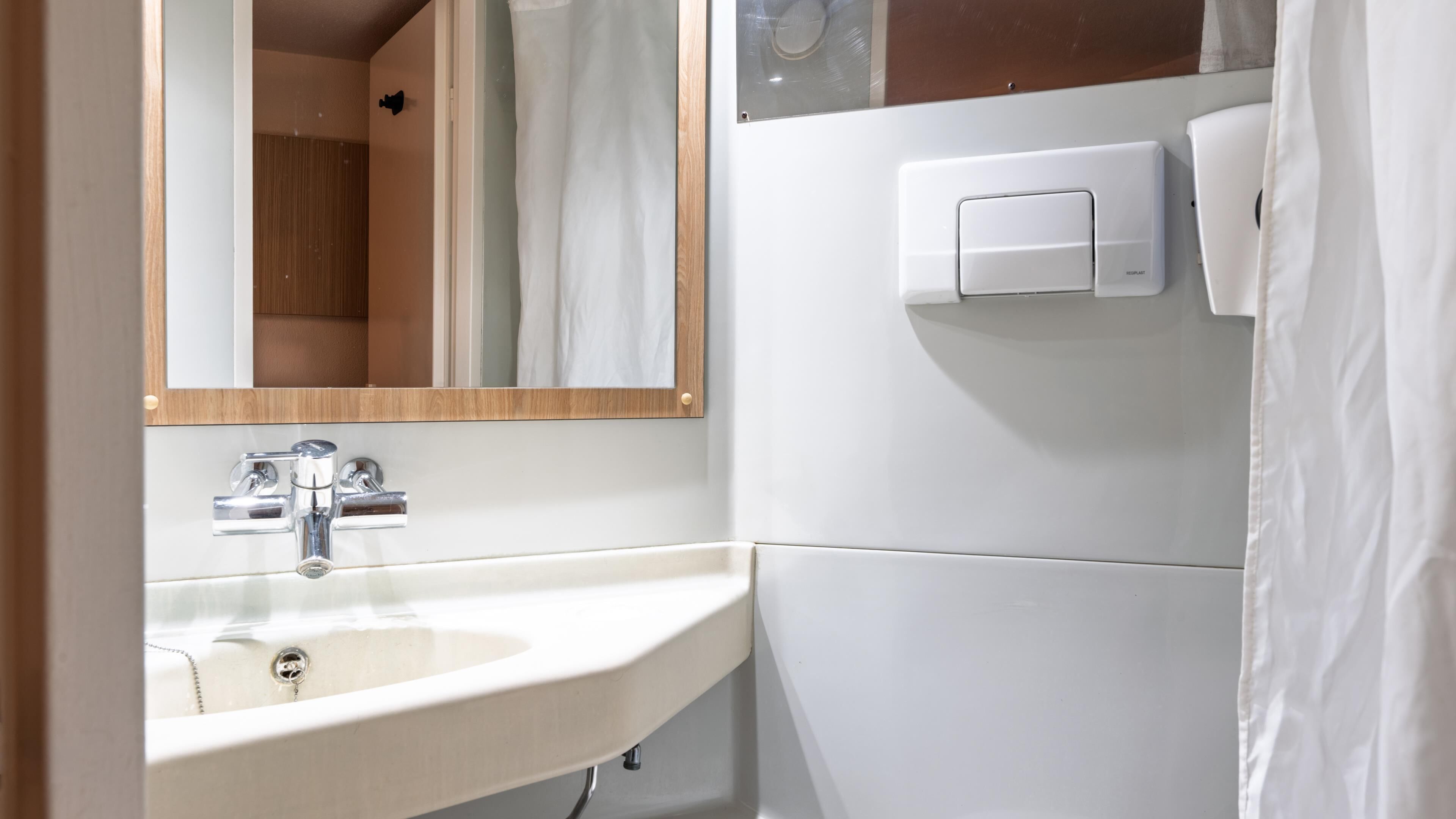 A bathroom with a sink, mirror, and towel dispenser.