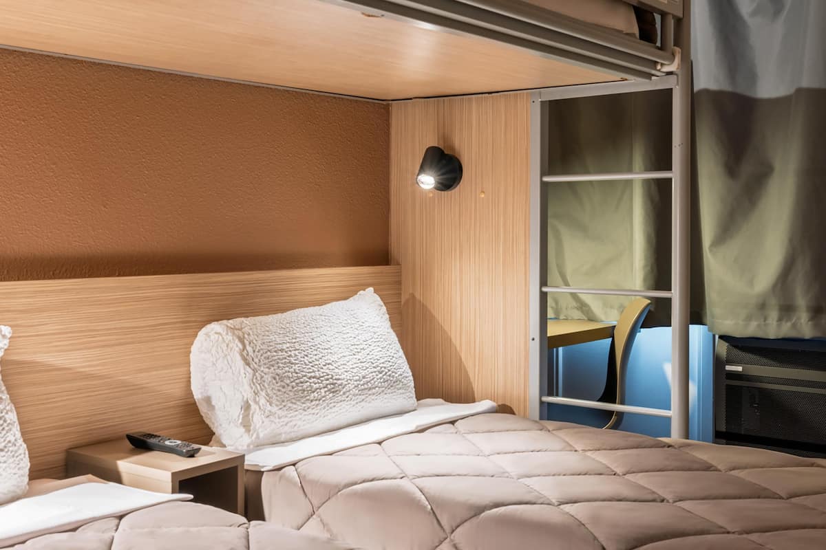 Hotelkamer met twee bedden, een nachtkastje met afstandsbediening, een wandlamp en een schuifdeur naar een balkon.