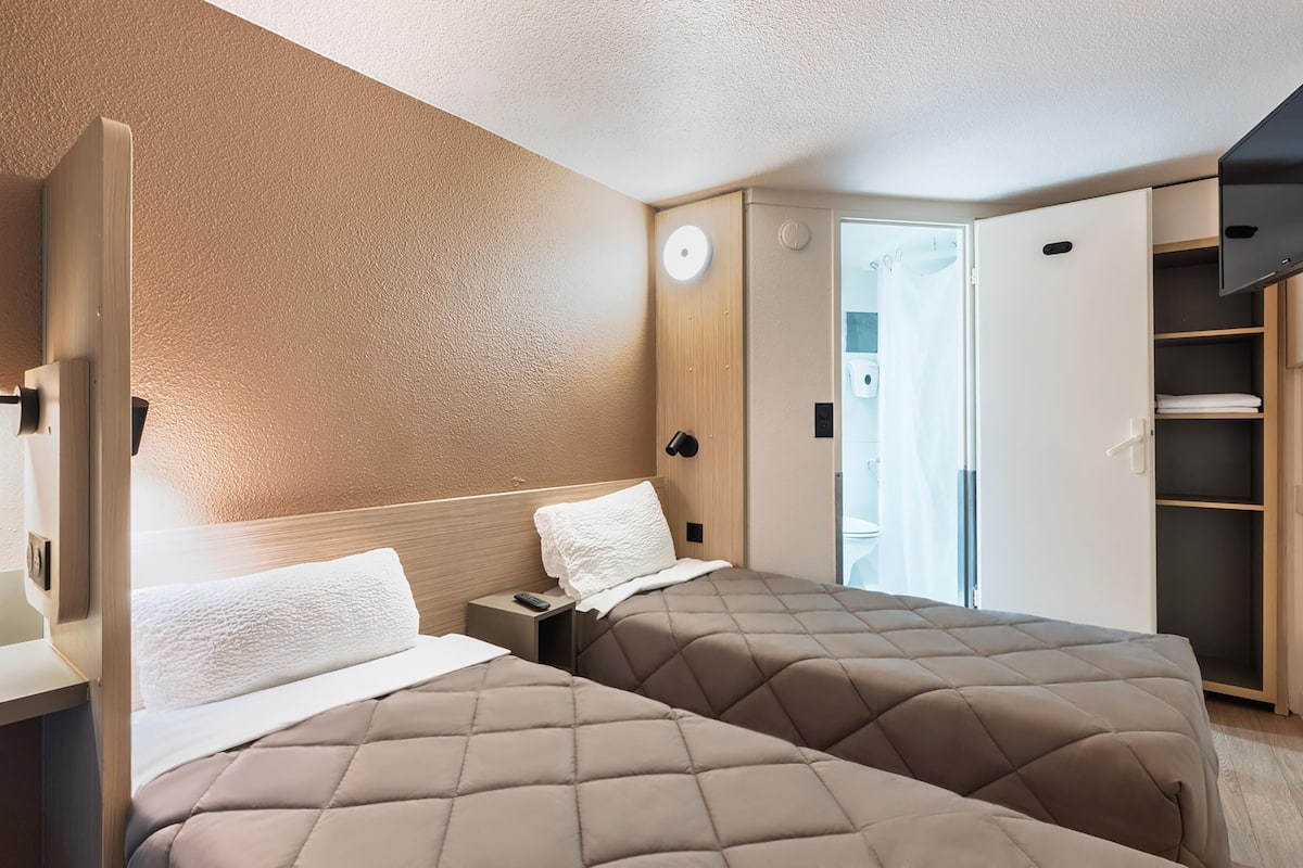 Een compacte hotelkamer met twee bedden, een kledingkast, een klein tafeltje en een televisie.