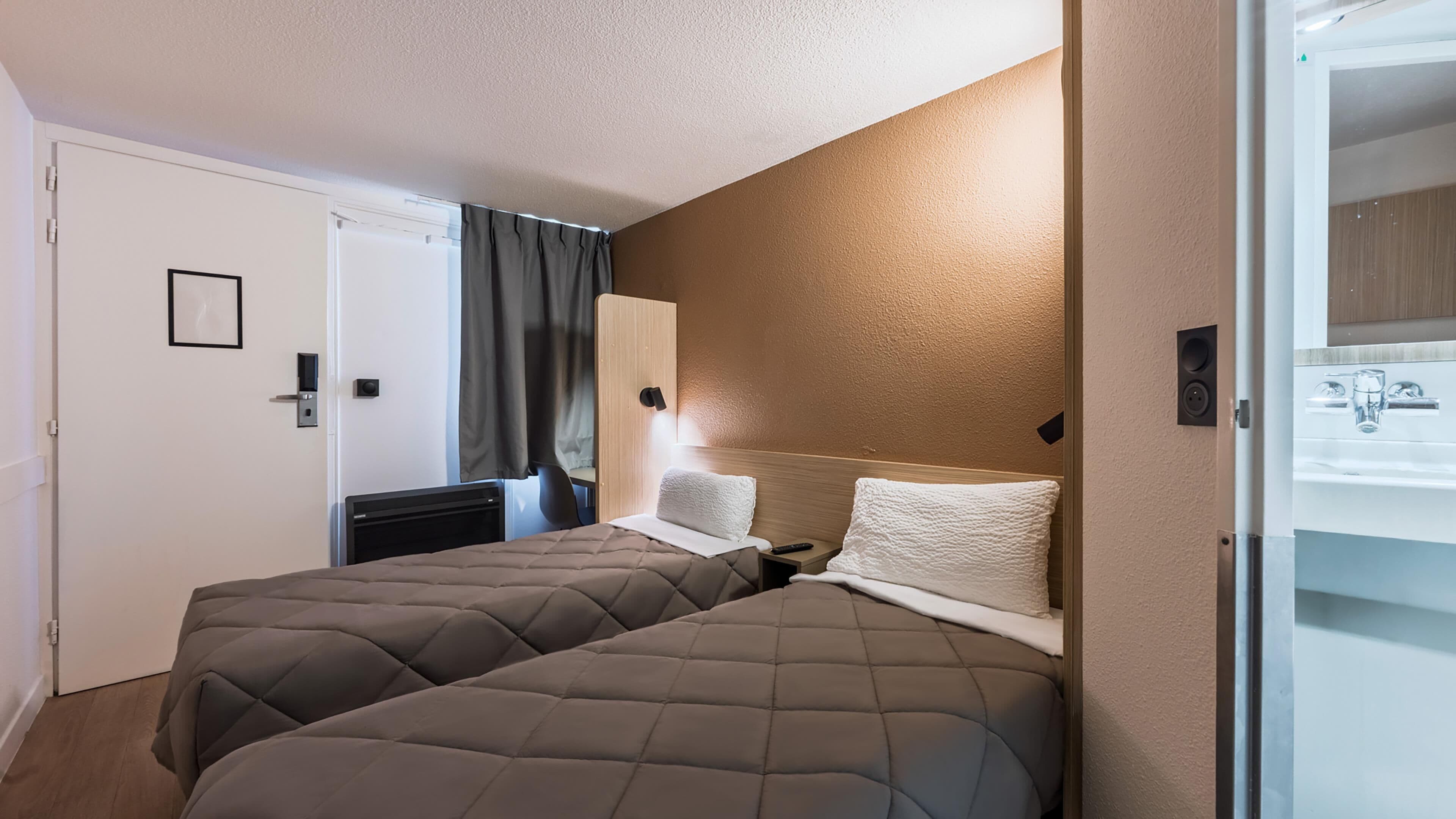 A hotel room with two beds, a bathroom with a sink, and a door leading to another room.
