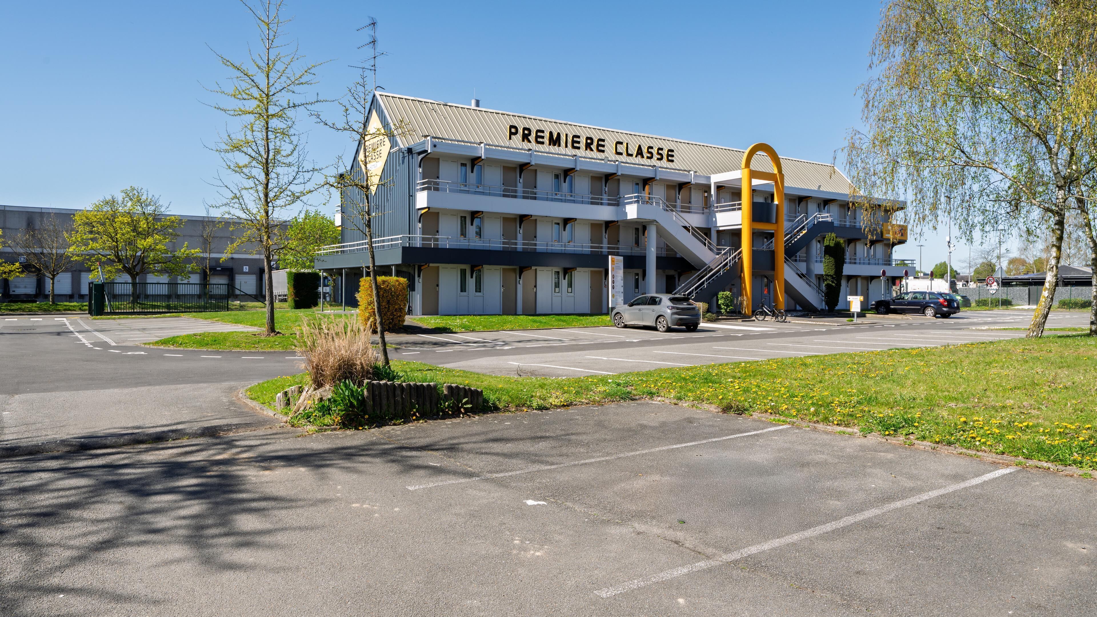 A building with 'PREMIERE CLASS' signage, a parking lot, and a clear sky.