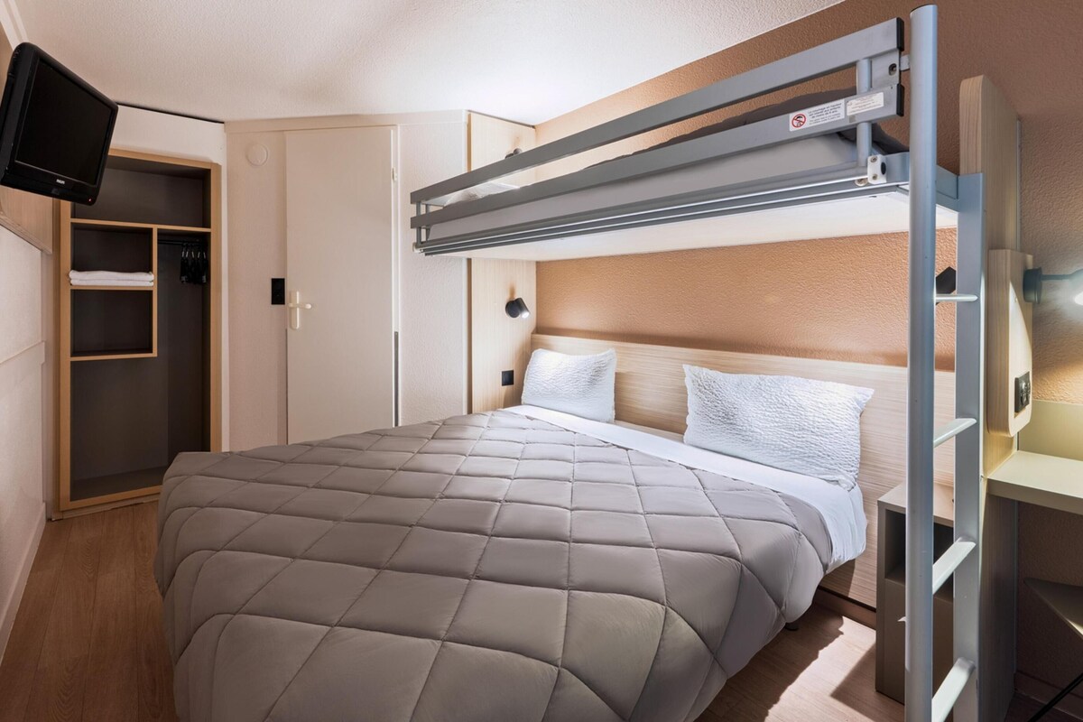 Un lit superposé avec une tête de lit, une table de chevet, un téléviseur à écran plat fixé au mur et une armoire avec un miroir.