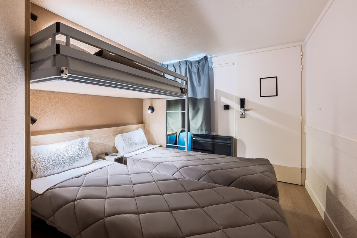 Une chambre d’hôtel avec un lit superposé, un bureau, une chaise et une porte coulissante.