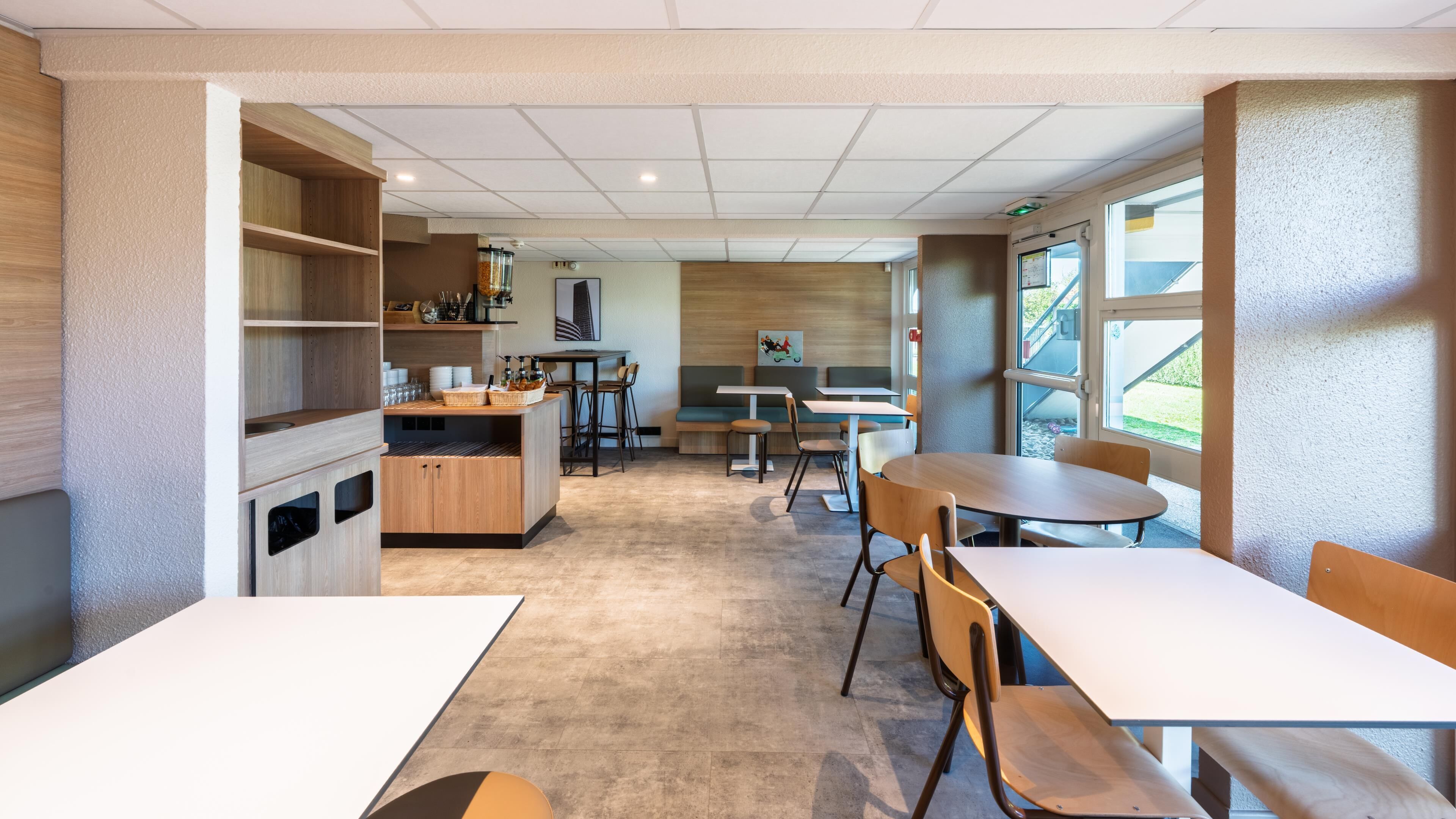 A modern cafe with wooden furniture, a counter with beverages, and a view of the outdoors.