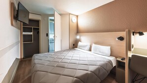 Una habitación de hotel con una cama, un armario, un escritorio y un televisor fijado en la pared.