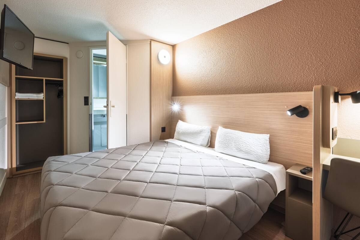 Een hotelkamer met een bed, een kledingkast, een bureau en een aan de muur bevestigde televisie.
