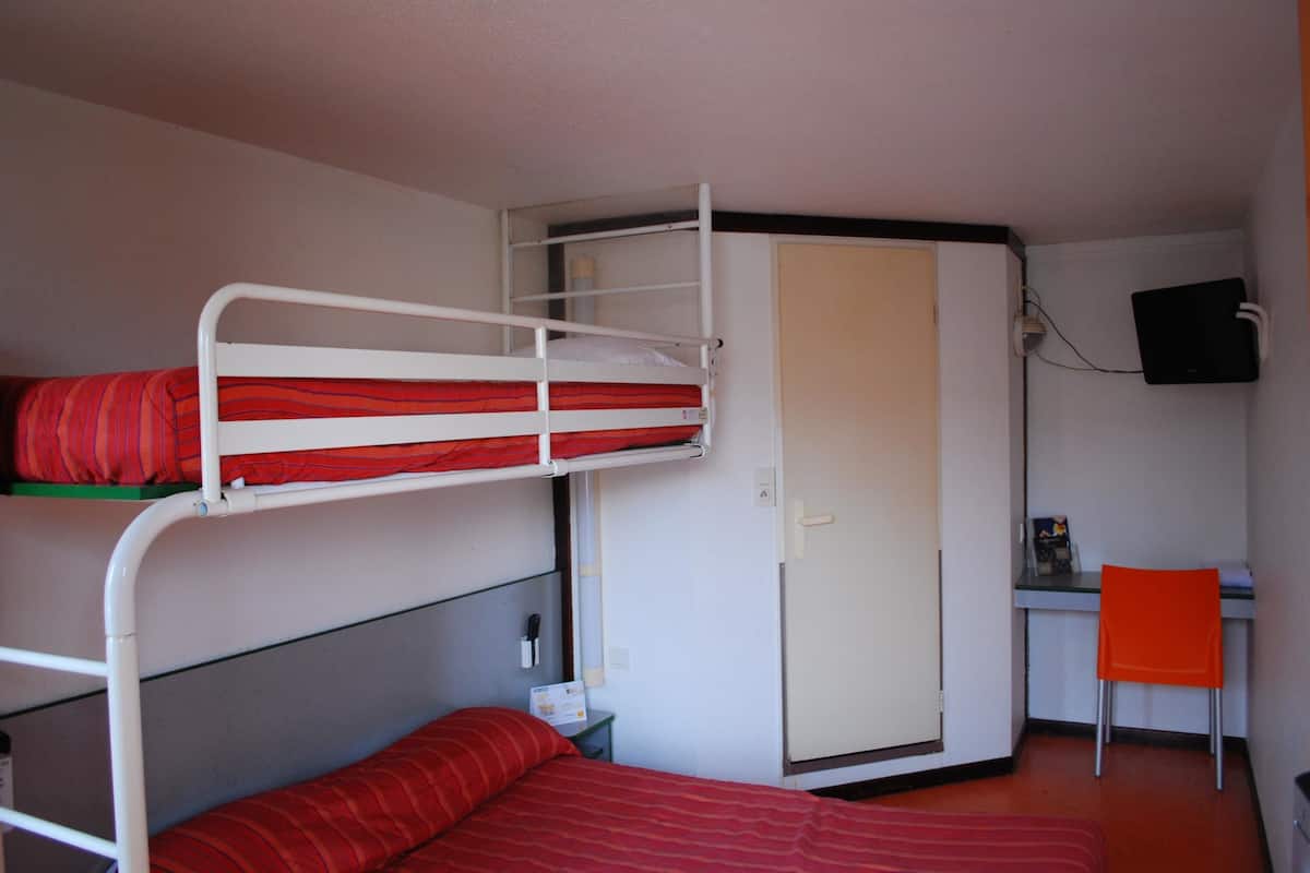 Une chambre avec un lit superposé, un bureau et une chaise, une armoire et un téléviseur.