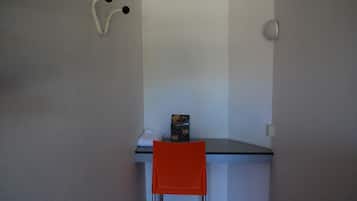 Een kleine kamer met een enkele oranje stoel, een wit bureau en een witte wand.