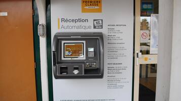 A hotel reception area with an automatic reception machine, a sign for Premier Classe Hotels, and a notice about reception hours.