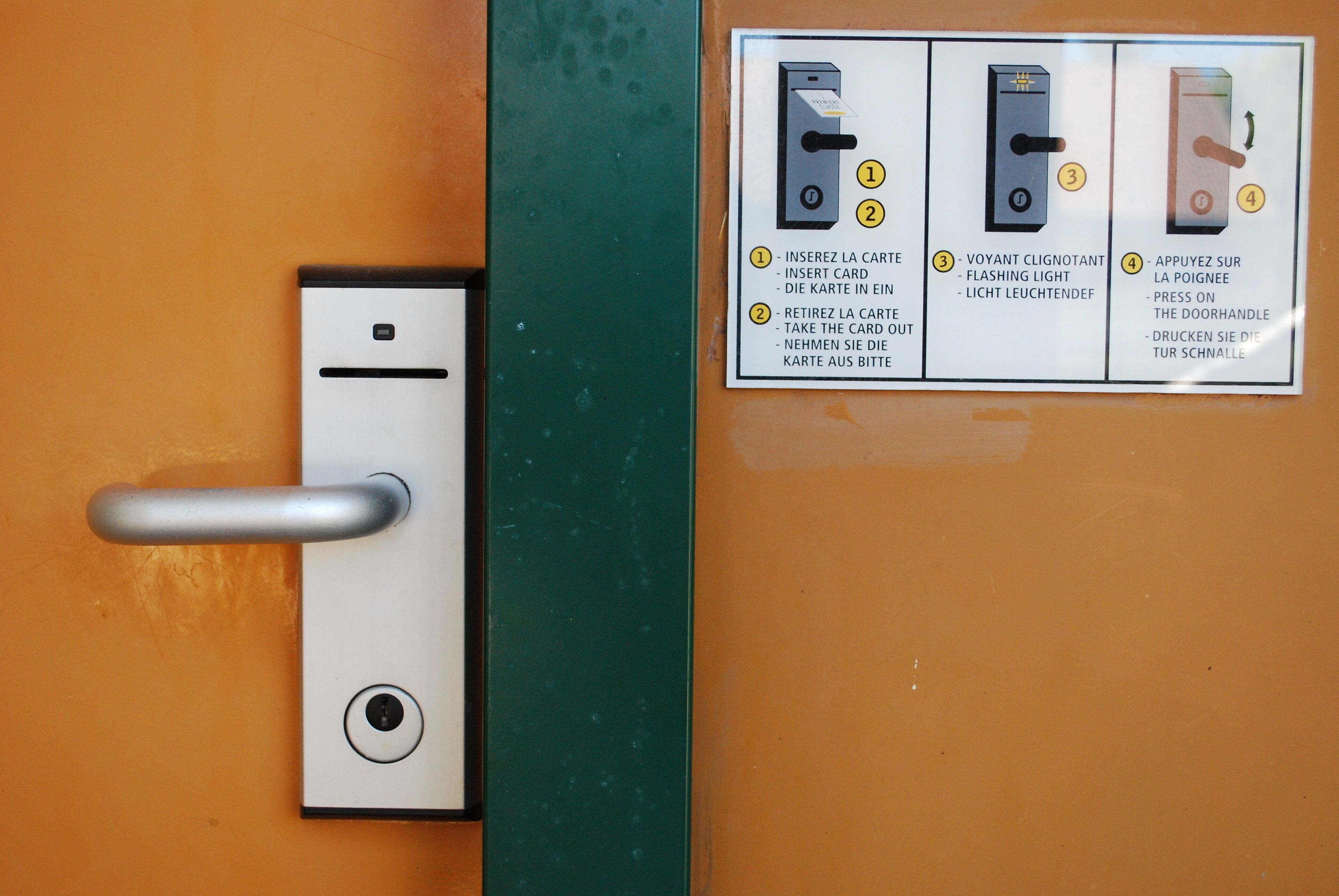 A door with a card reader and instructions in multiple languages.