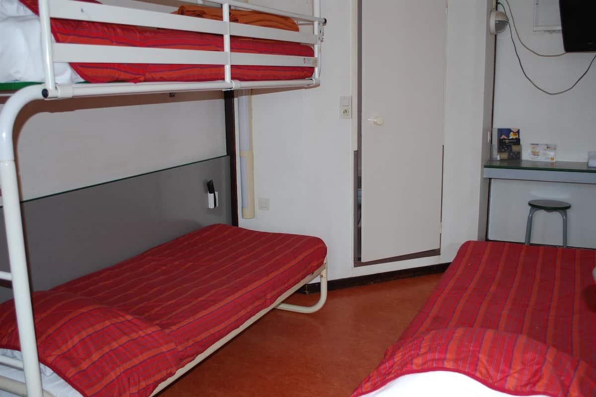 Une chambre avec un lit superposé, un bureau et une chaise, une porte et un petit tabouret.