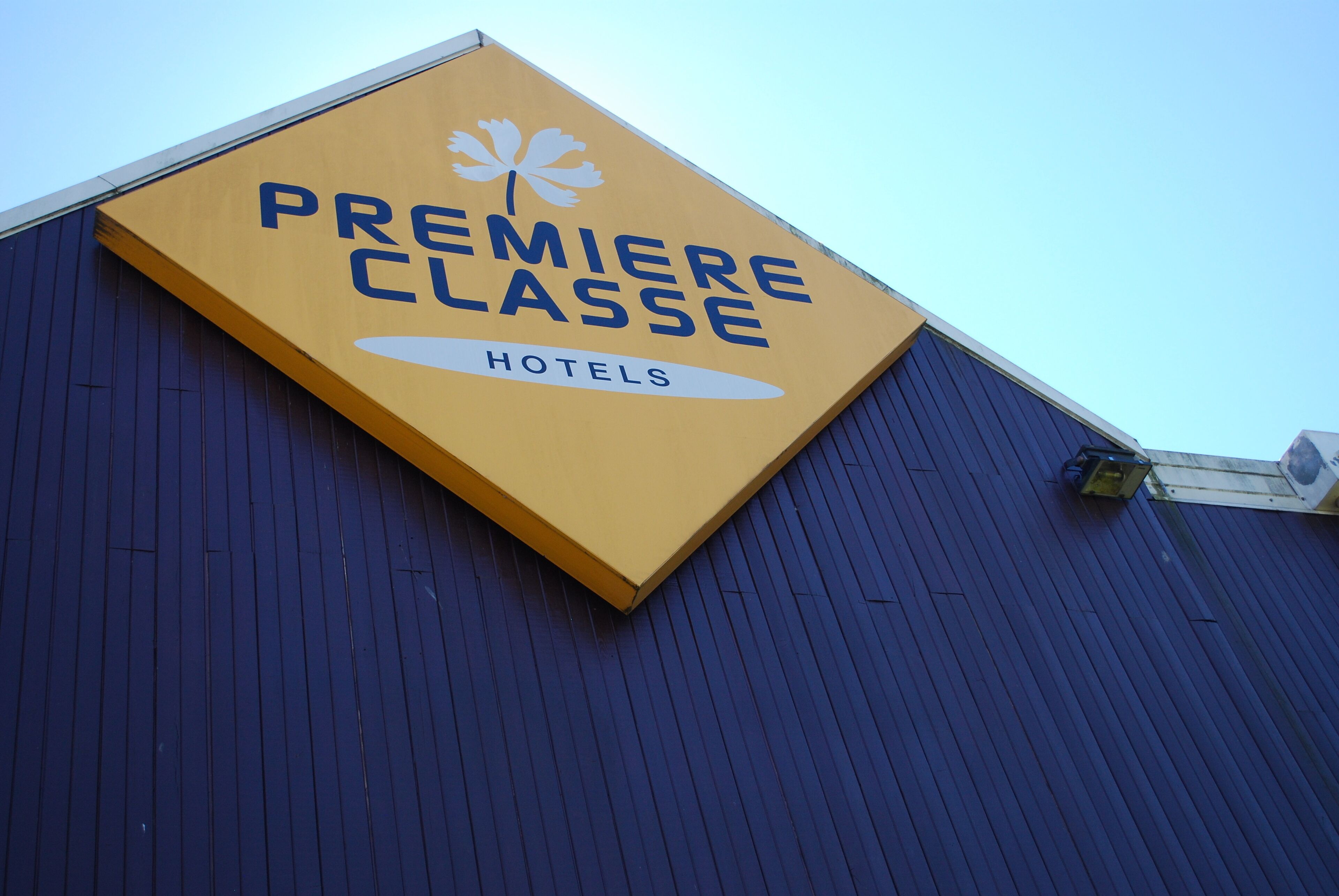 A yellow sign with "Premiere Classe Hotels" and a maple leaf logo on a blue building.