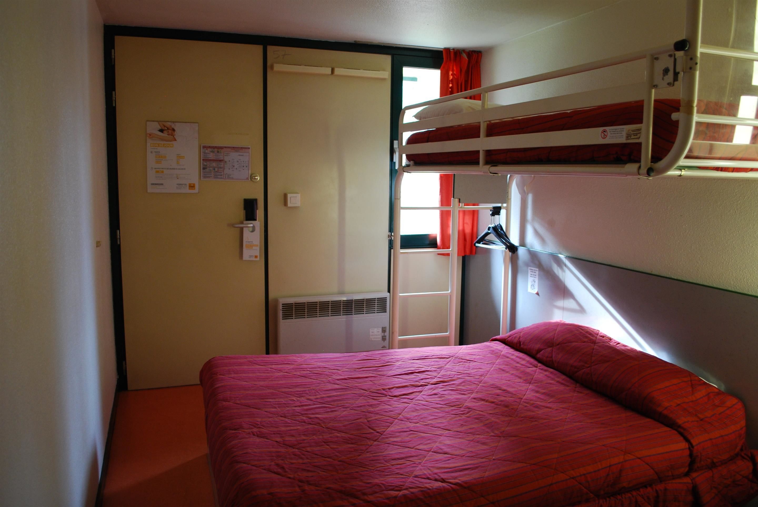 A compact hotel room with a bunk bed, a single bed, a door with a notice, and a window with curtains.
