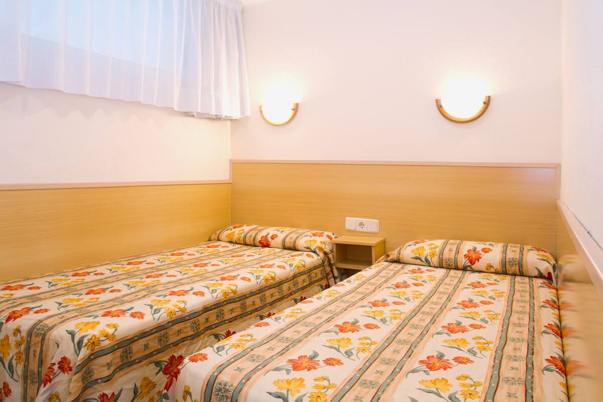 Una habitación con dos camas, cada una con ropa de cama floral, cabeceros de madera y dos lámparas de pared.