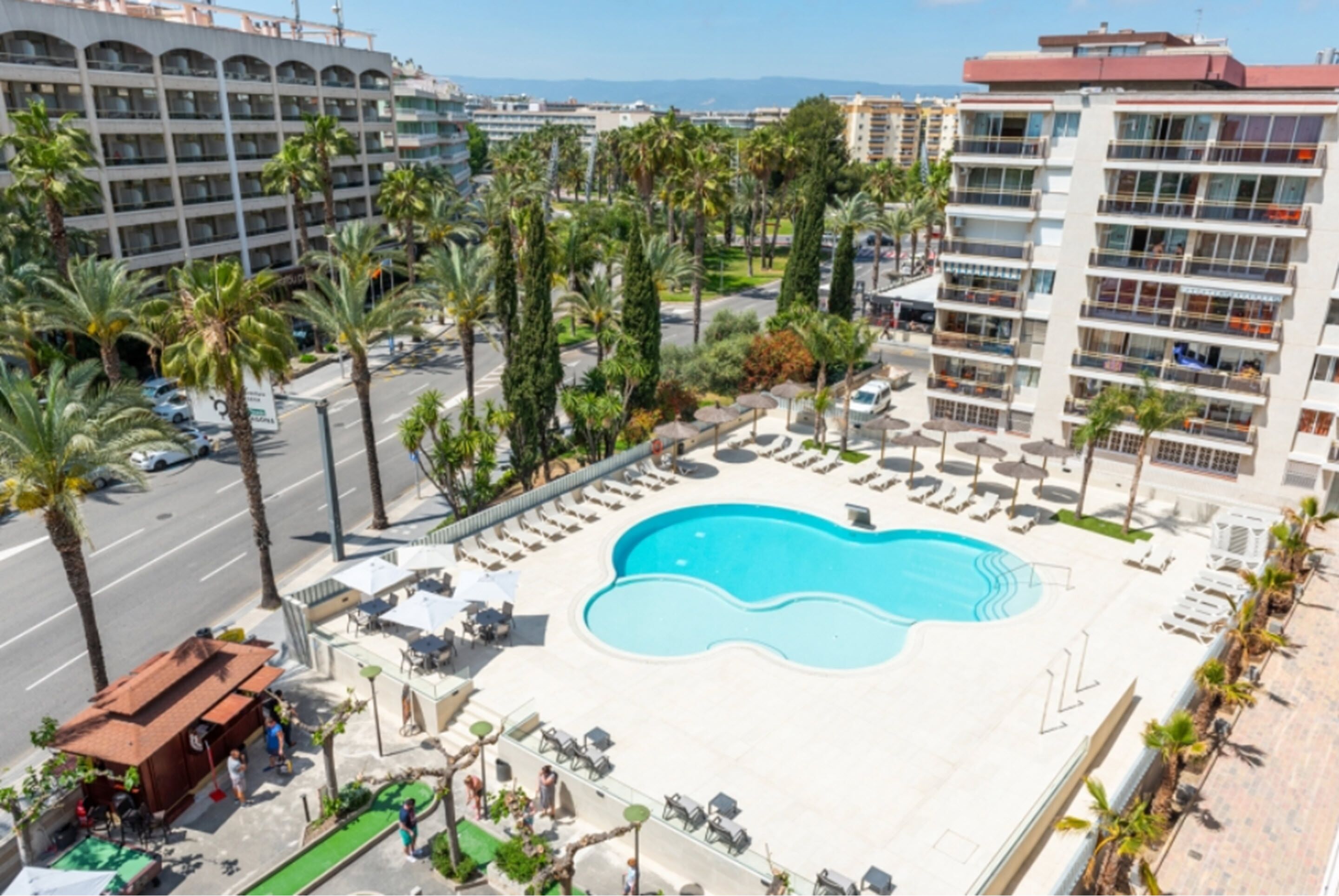 A hotel with a large swimming pool surrounded by palm trees and lounge chairs.