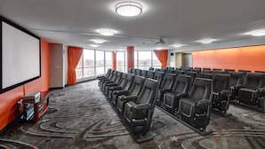 Uma sala de conferências com fileiras de cadeiras pretas, uma tela grande e um carpete com padrão circular.