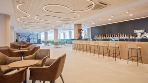A modern bar area with a long counter, multiple stools, and a ceiling with unique lighting. - Hotel Best Mediterraneo (Salou)