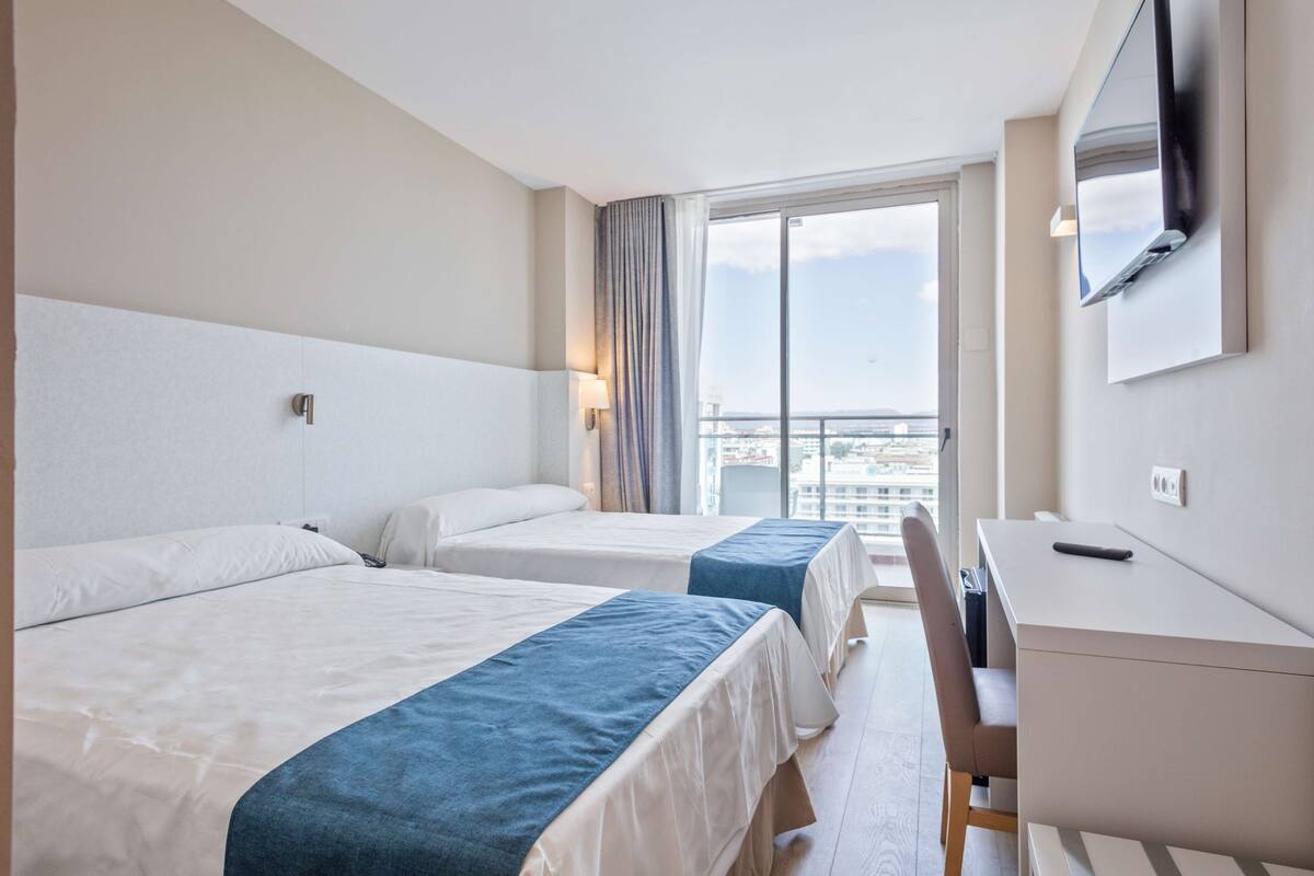 A hotel room with two beds, a desk, and a TV.