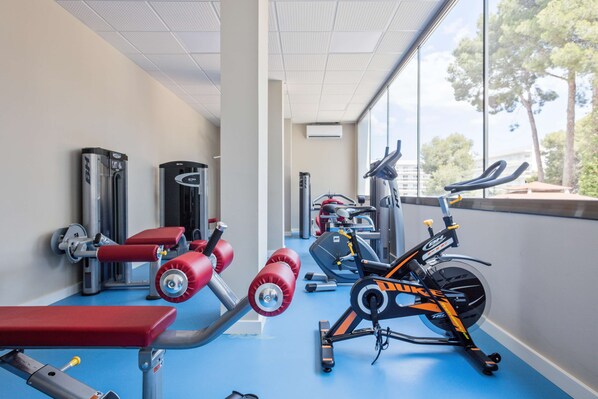 Une salle de sport équipée de divers appareils d’exercice, notamment un banc, des haltères et un appareil de musculation elliptique.