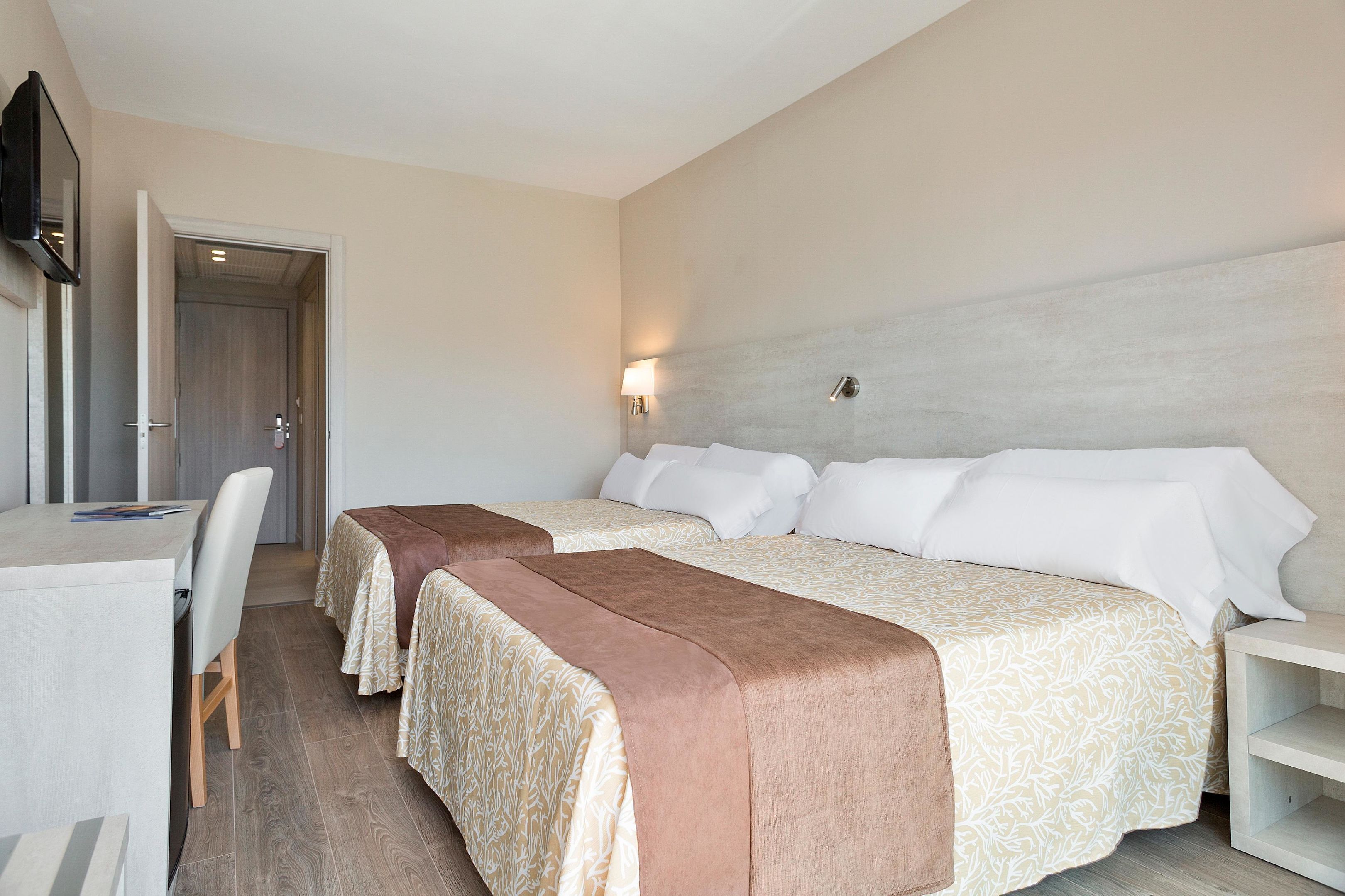 Habitación de hotel con dos camas, un escritorio y un televisor.