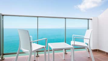 A balcony with two white chairs and a small table, overlooking a turquoise sea and distant mountains.