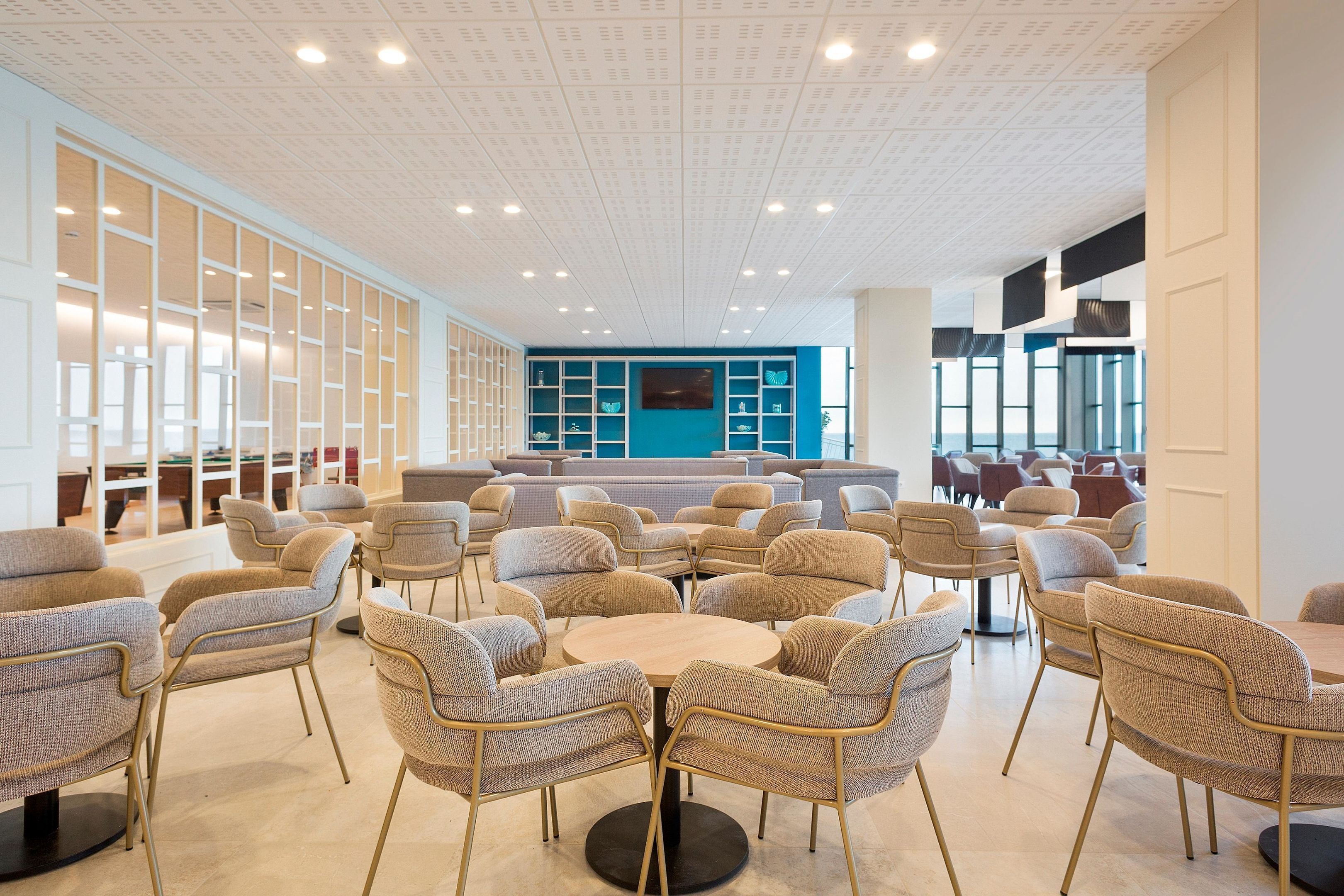 Et moderne loungeområde med runde borde og komfortable stole, en blå væg og et loft med indbygningsbelysning.