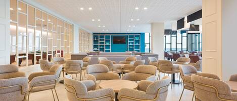 Et moderne loungeområde med runde borde og komfortable stole, en blå væg og et loft med indbygningsbelysning.