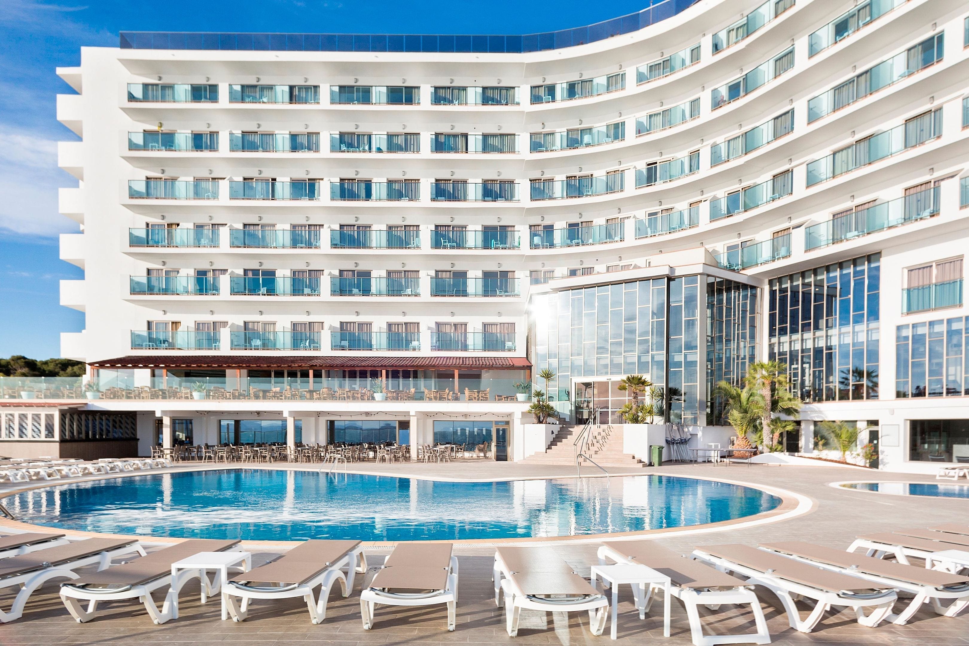 Un hotel moderno con un amplio espacio de piscina, varios balcones y vista despejada al océano.