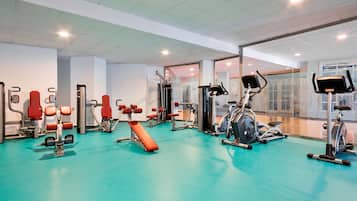 Un gimnasio con diverso equipo de ejercicio, incluyendo cintas de correr y máquinas de pesas, sobre un piso turquesa.