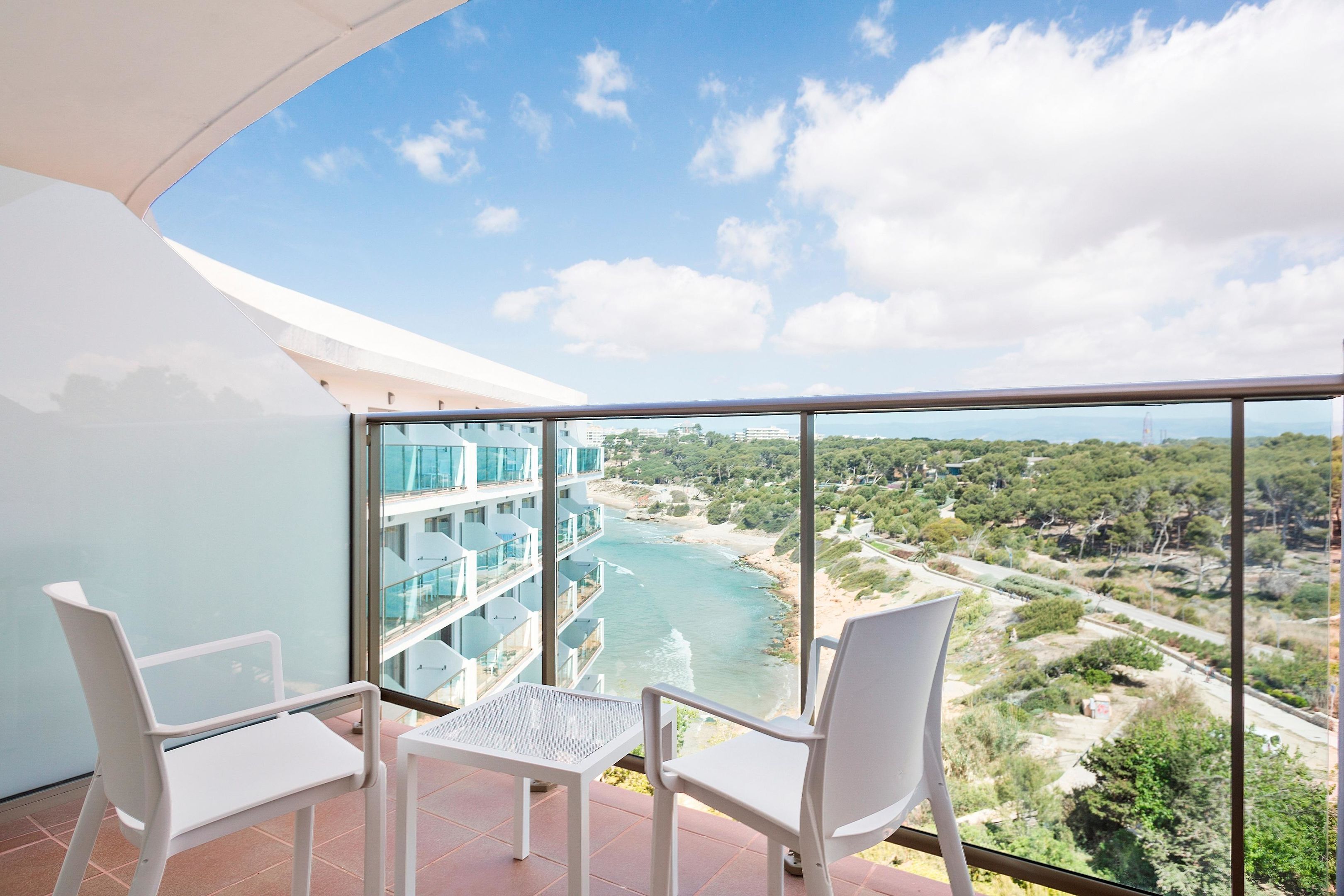 A balcony with two white chairs and a small table, overlooking a river and buildings.