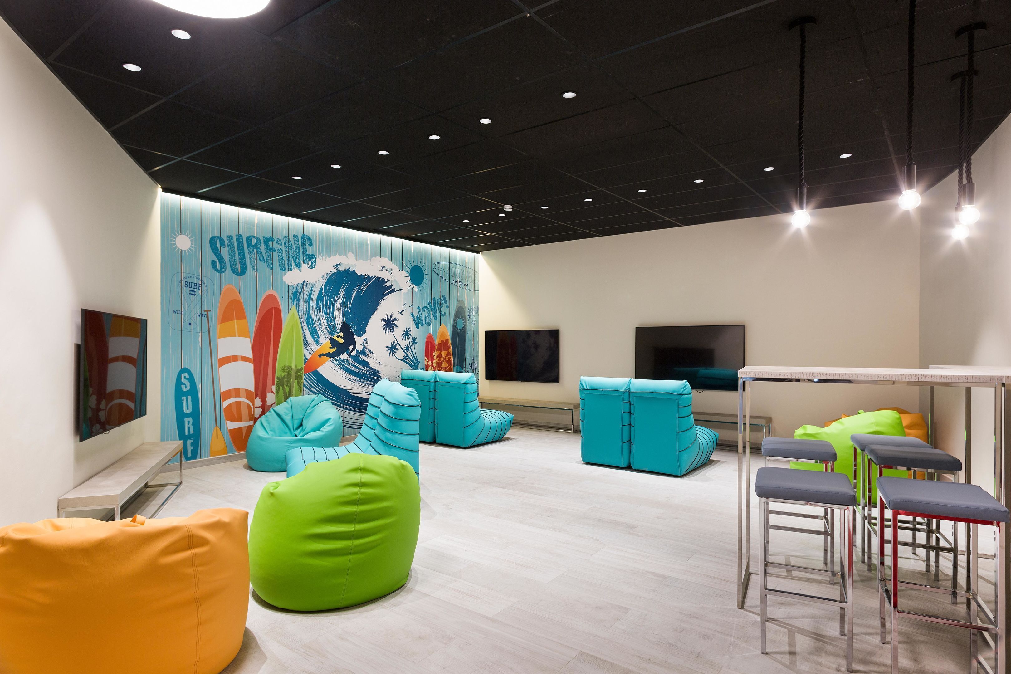 A modern indoor space with a surf-themed mural, colorful bean bags, and bar stools.