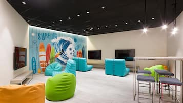 A modern indoor space with a surf-themed mural, colorful bean bags, and bar stools.