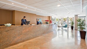 A modern reception area with a marble counter, a receptionist, and a seating area with chairs and a table. - Hotel Best Negresco (Salou)