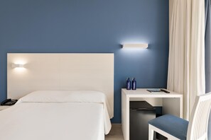 A hotel room with a bed, bedside table, and a chair. There is a phone on the bed, a remote control, and two water bottles on the table. - Hotel Best Oasis Park (Salou)