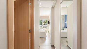 Un pasillo de hotel con una puerta de madera, una pared blanca y vistas a un balcón con mobiliario exterior.