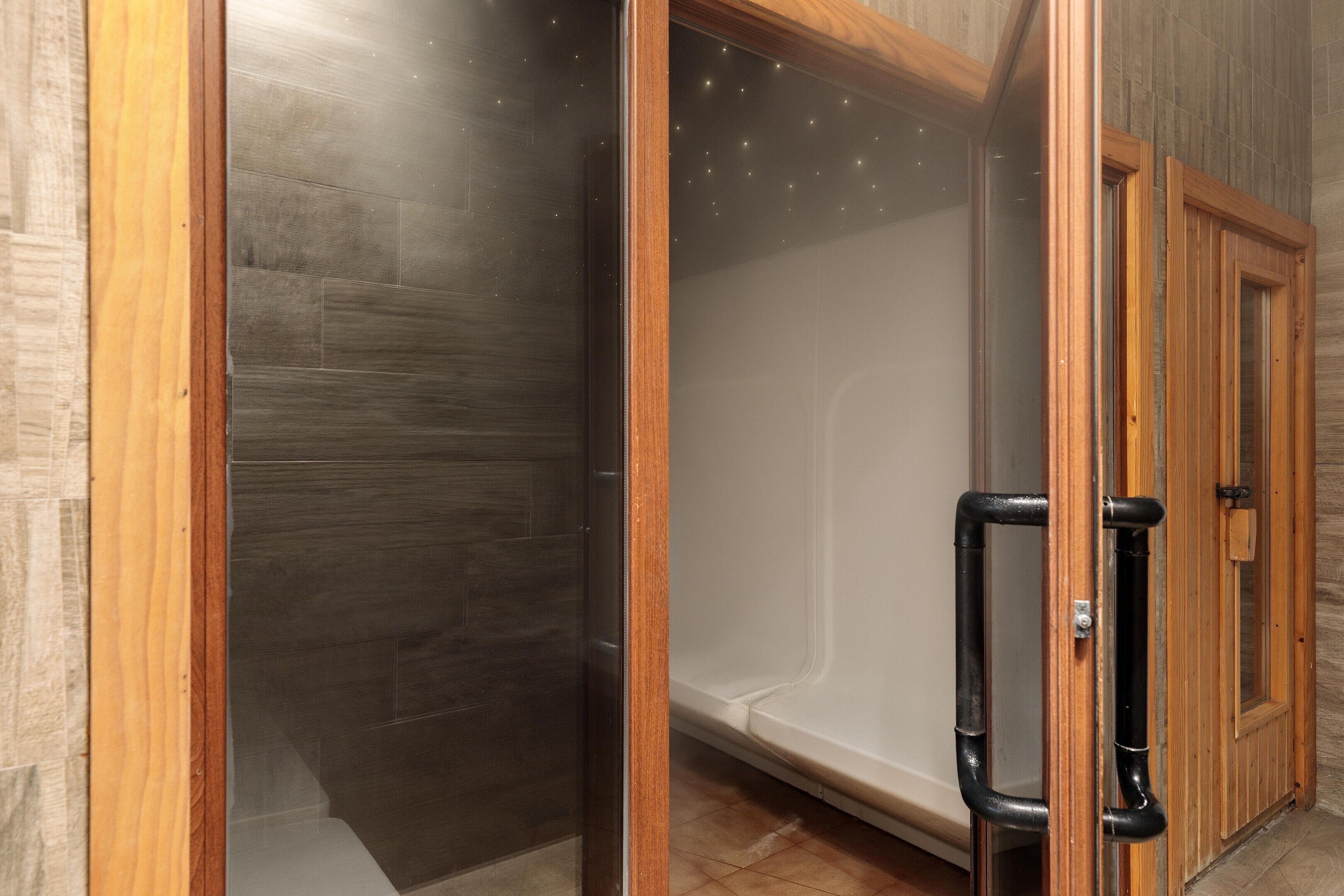Baño con cabina de ducha de vidrio, marco de puerta de madera y grifería de ducha negra.