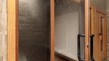 Baño con cabina de ducha de vidrio, marco de puerta de madera y grifería de ducha negra.