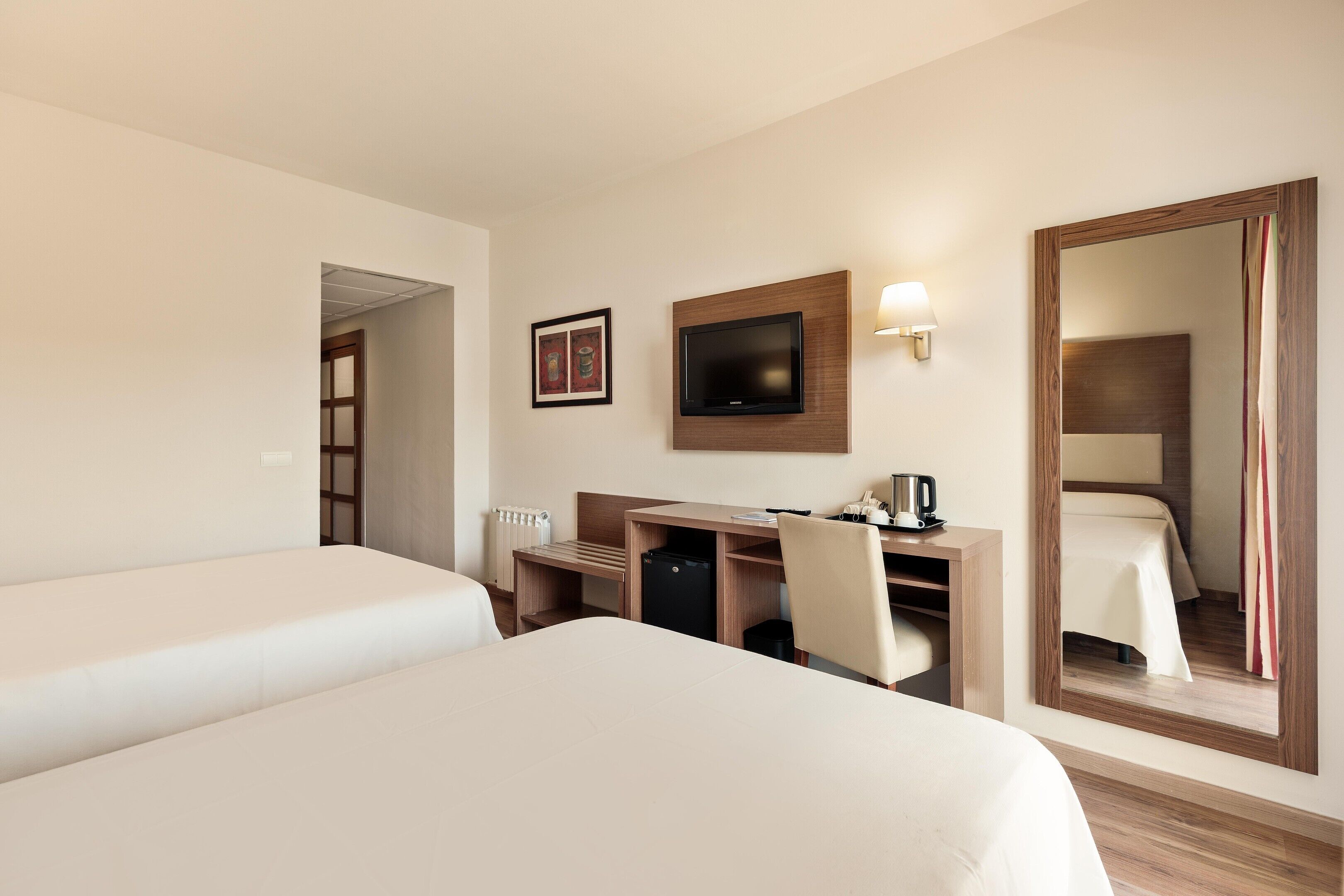 A hotel room with a bed, a desk, a chair, a television, and a mirror.