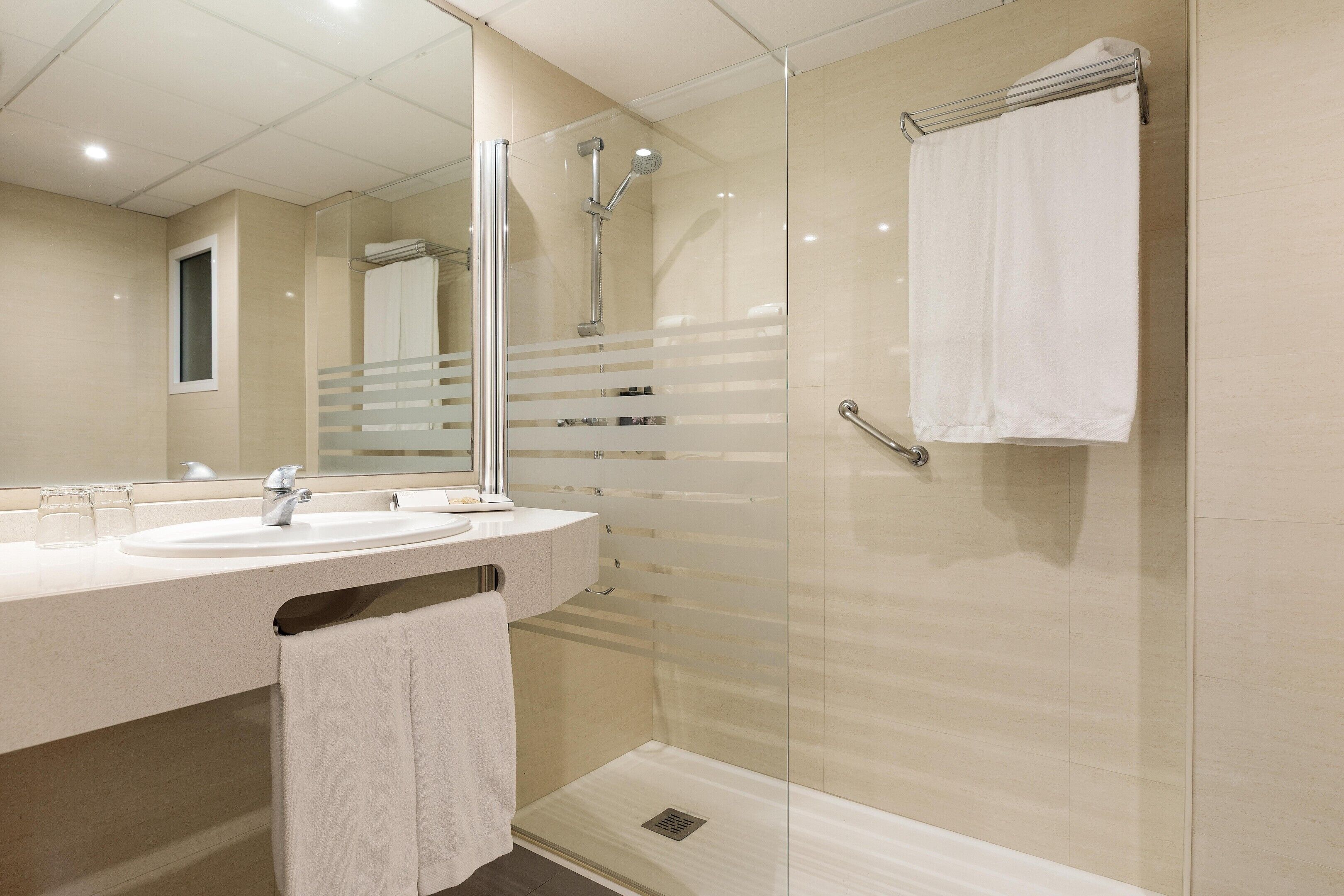 Un baño moderno con ducha envuelta en vidrio, un lavamanos con espejo y un perchero para toallas.