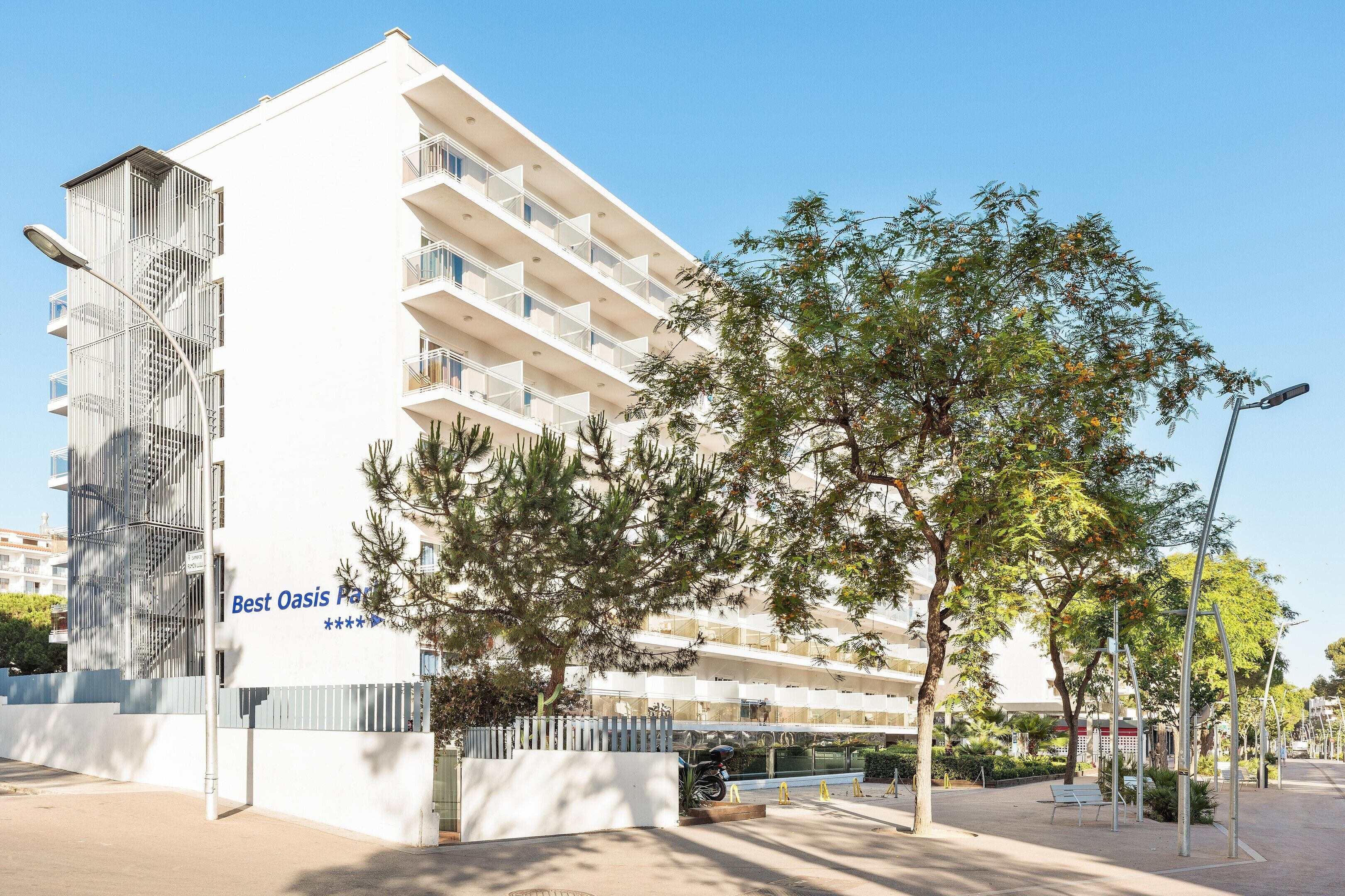 Een hotel met meerdere verdiepingen, balkons, een poort en een heldere lucht.