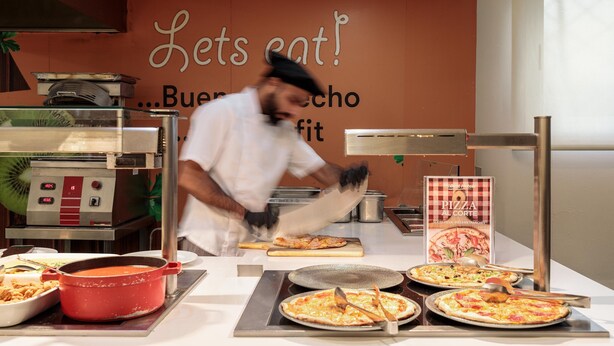 A kitchen area with a chef preparing food, a pizza station with multiple pizzas, and a sign that reads 'Let's eat!' - Hotel Best Oasis Park (Salou)