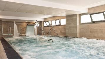 A large indoor swimming pool with a slide, multiple windows, and a high ceiling.