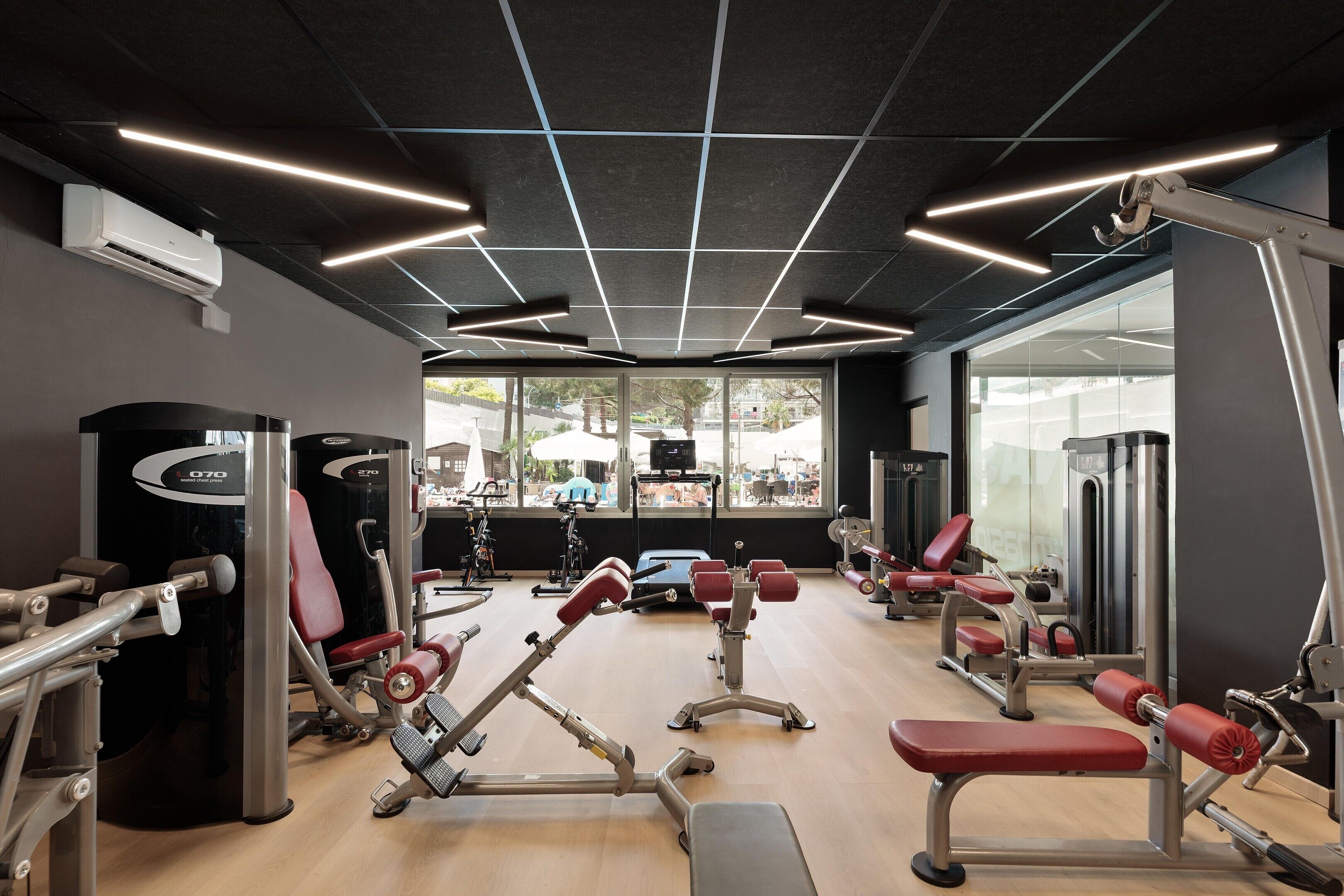 A gym with various exercise equipment, large windows, and a modern ceiling design.