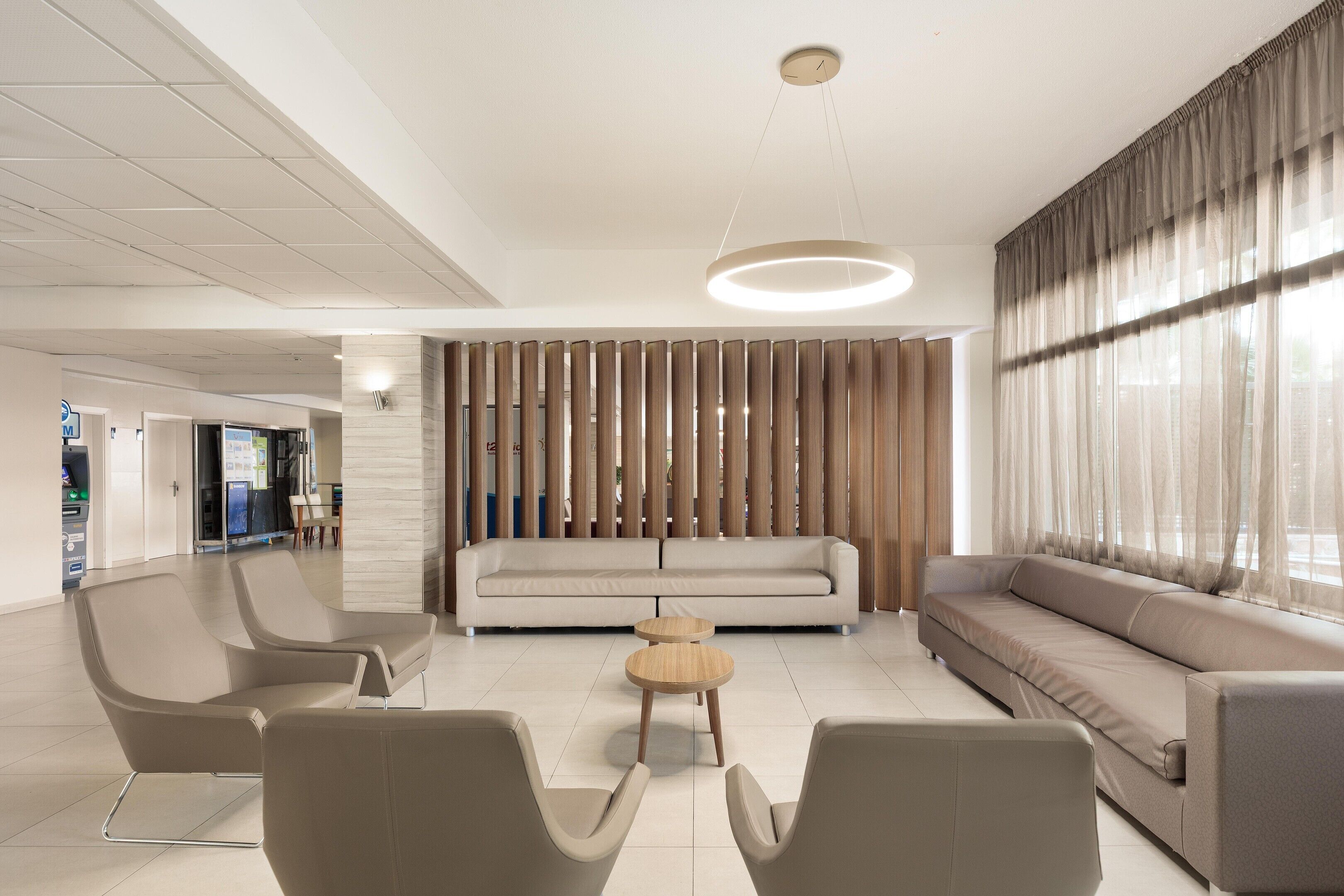 Un moderno vestíbulo de hotel con un sofá, sillas, una mesa redonda y una pared decorativa.